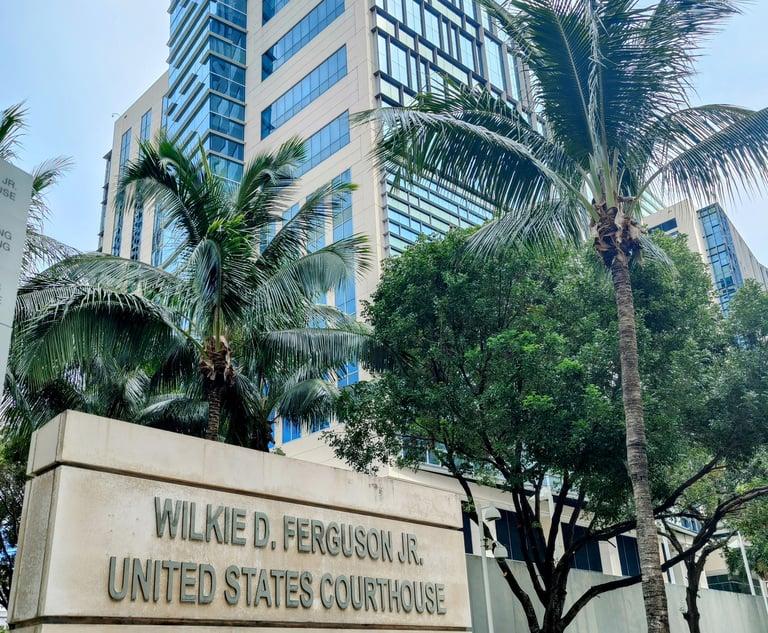 Stone sign for the Wilkie D. Ferguson Jr. United States Courthouse in front of palm trees and a glass federal building in Miami.