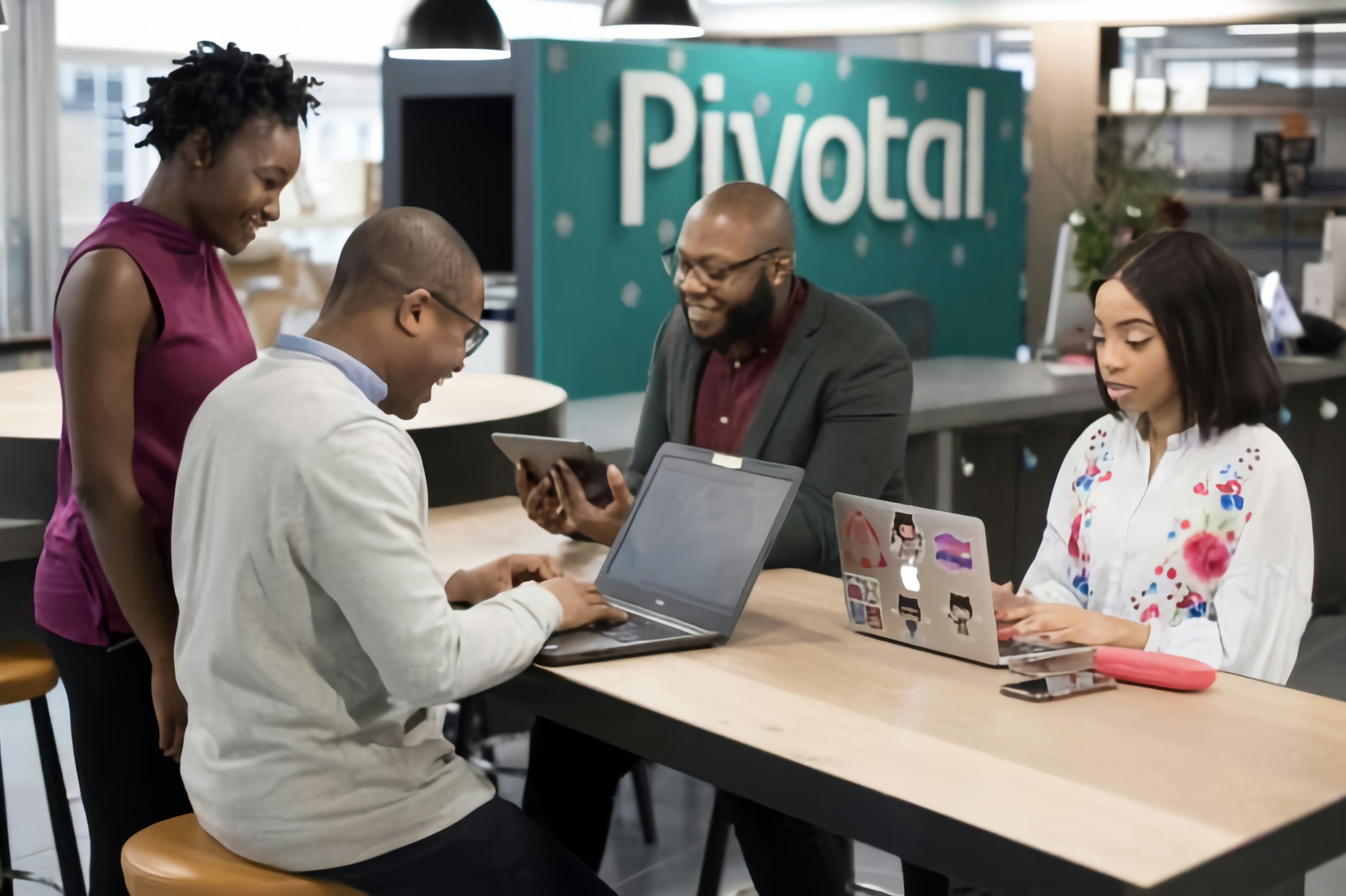 Business professionals work together on laptops around a shared office table.