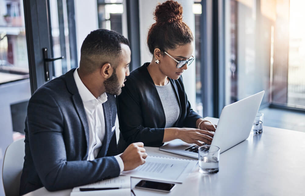 Two legal professionals review documents and information together on a laptop.