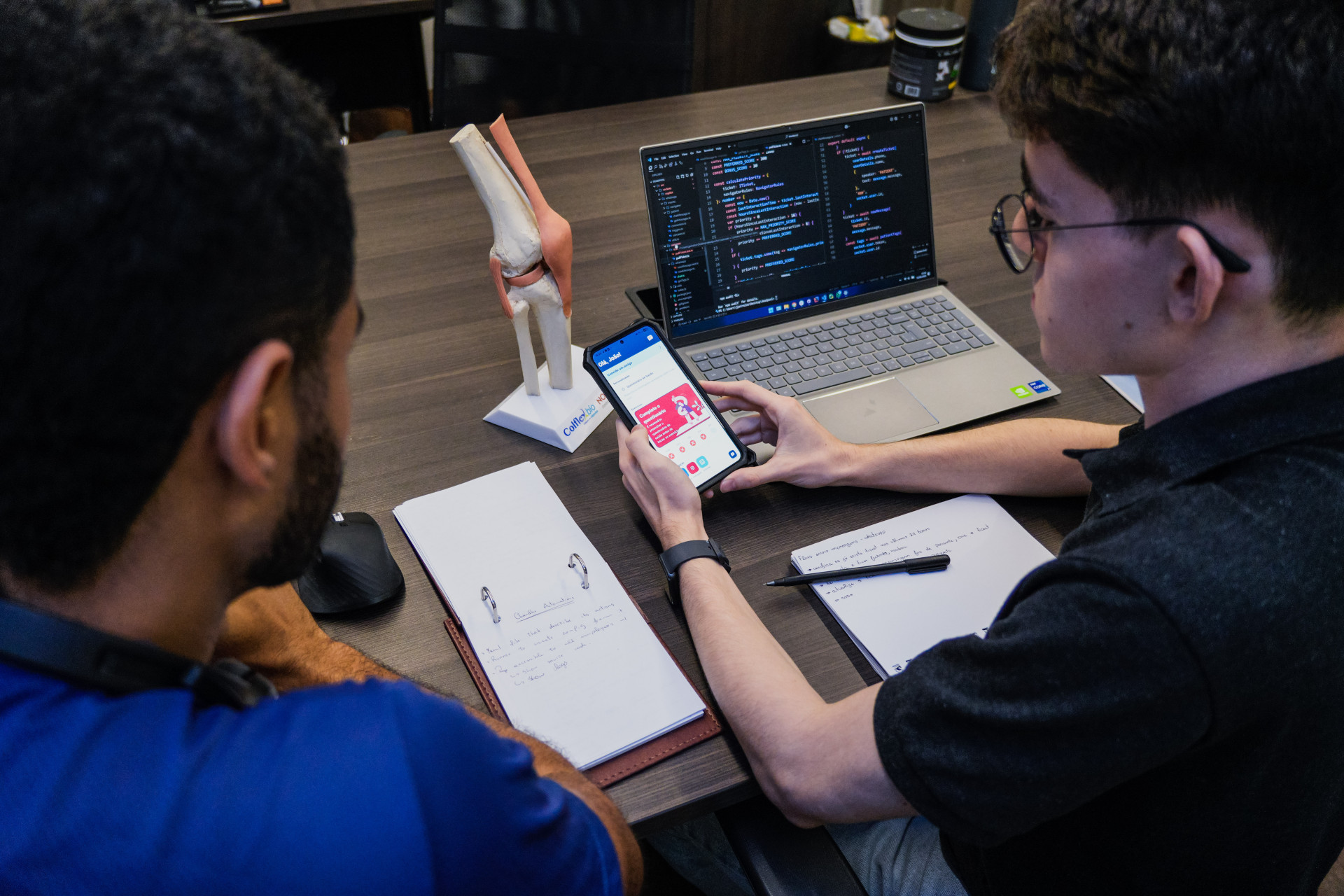 Developer tests an interactive mobile interface beside code on a laptop during accessibility review.